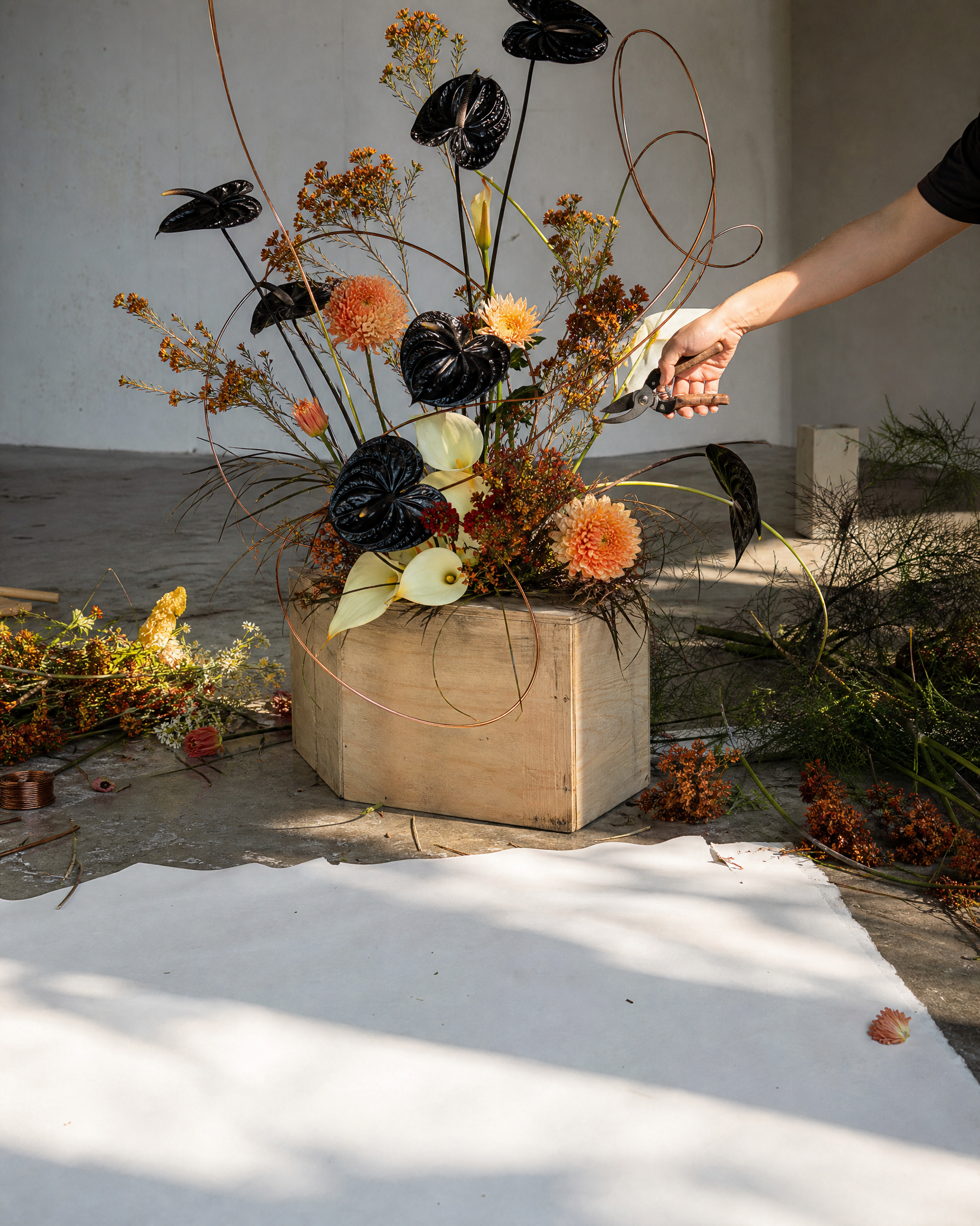 A florist cuts a black and orange structure on a plywood block