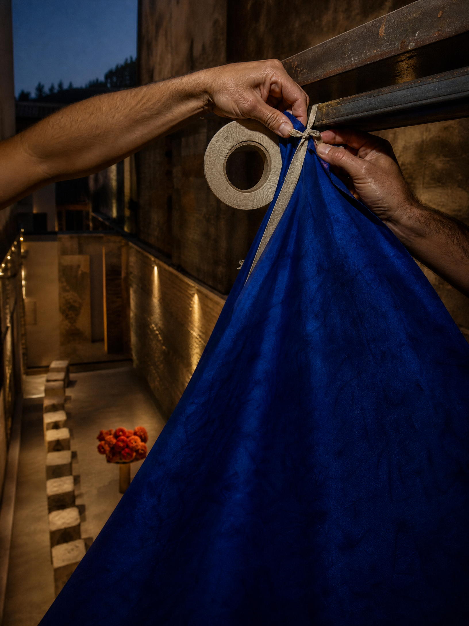 Hands tie a bright blue canopy to a steel beam at blue hour