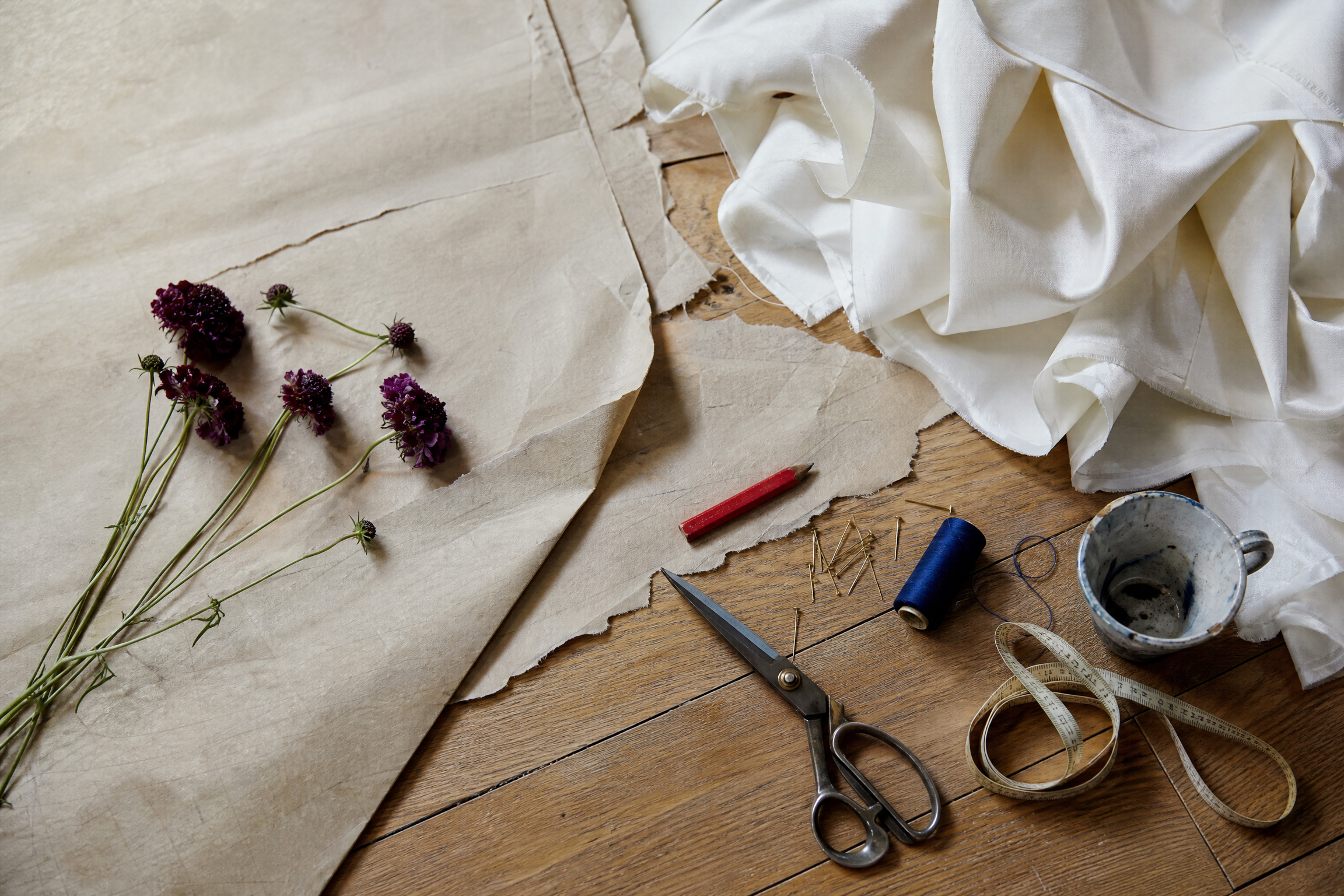 Linen, scissors, flowers, pins, and pencil spread over oak