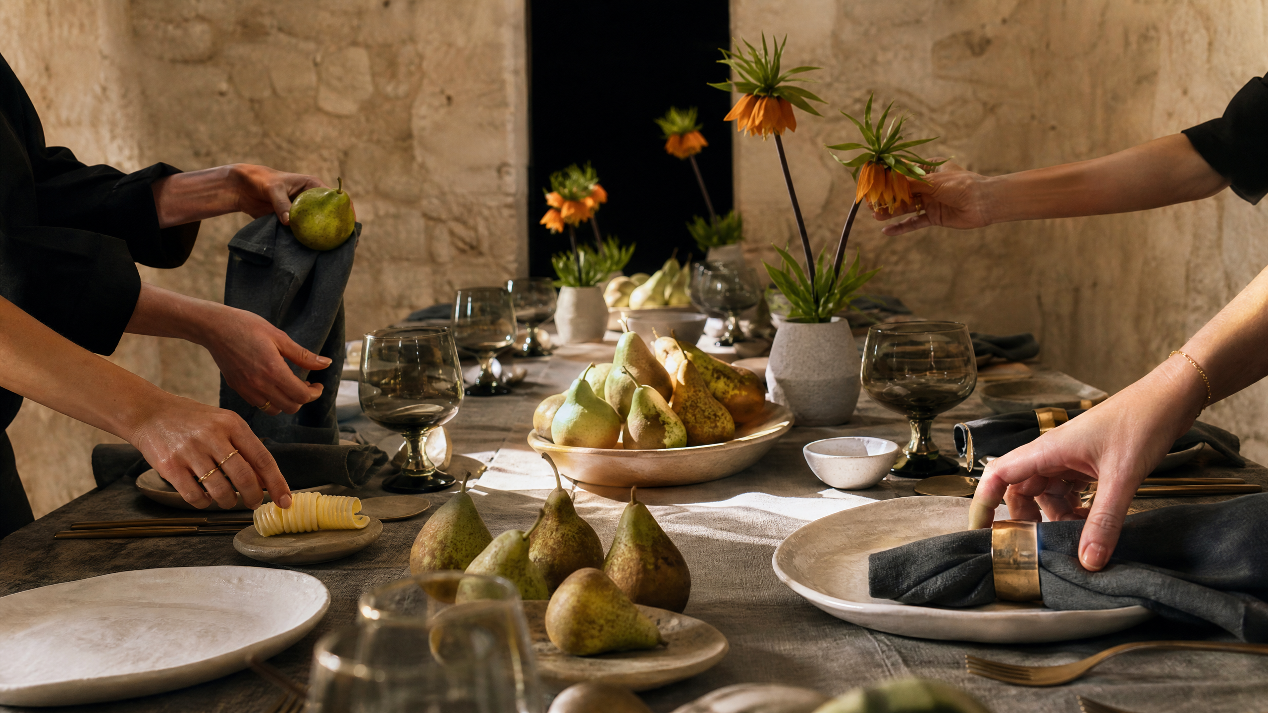 Hands refining a pear, butter, napkin, and flower on a linen-covered table